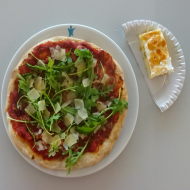 Hausgebackene Rucola-Pizza mit Schinkenstreifen und gehobeltem italienischen Hartkäse (2,19,22,49,51,81) + 1 Stück Landfrauenkuchen (15,18,19,81)